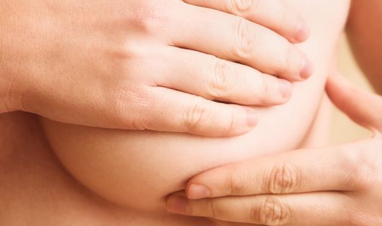 Woman hand checking lumps on her breast for signs of breast cancer on gray background. Healthcare concept.